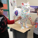 students stamp thumbprints onto cat statue