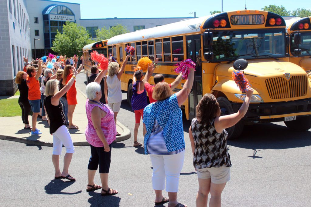 teachers wave goodbye as busses roll out of elementary school parking lot