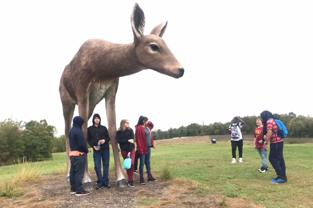 students pose with deer sculpture