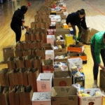 three girls pack long line of bgs with food on gym floor