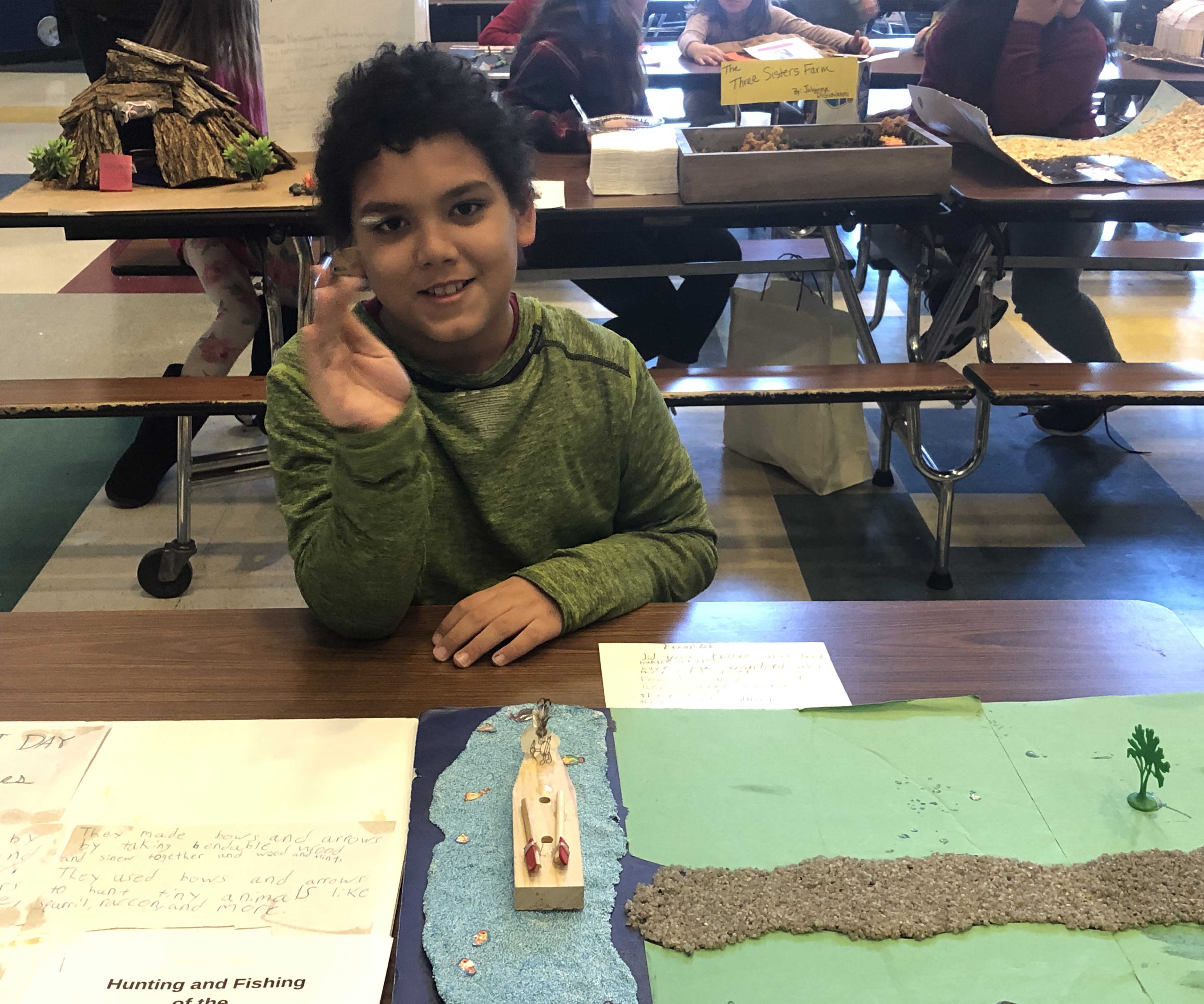 boy sitting at table with Native American diorama of river and fishing