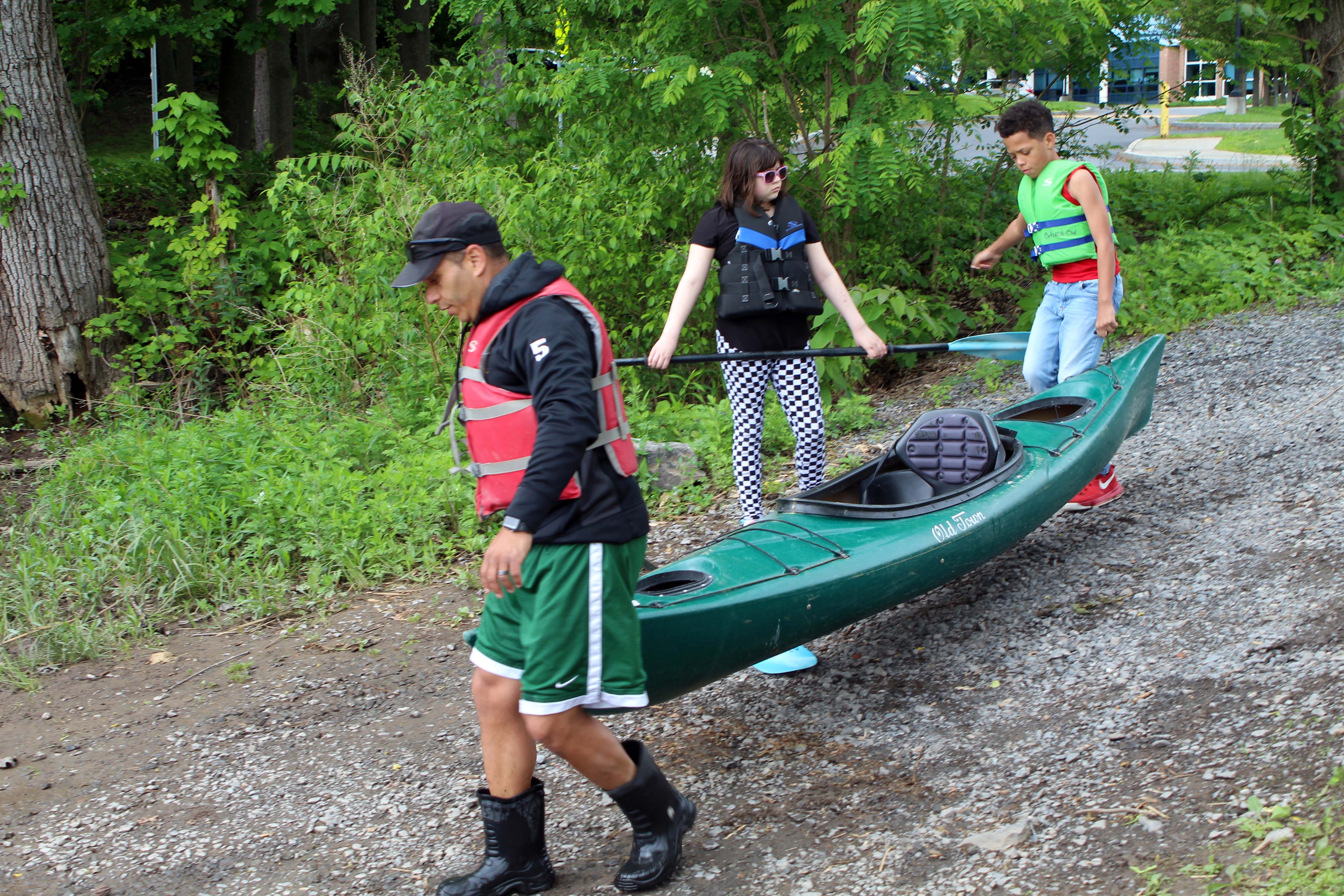 teacher and two students carry kayak to water