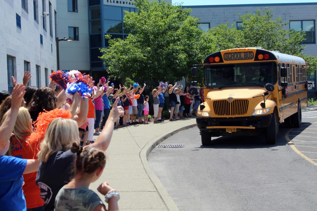 staff wave to bus as it leaves the parking lot
