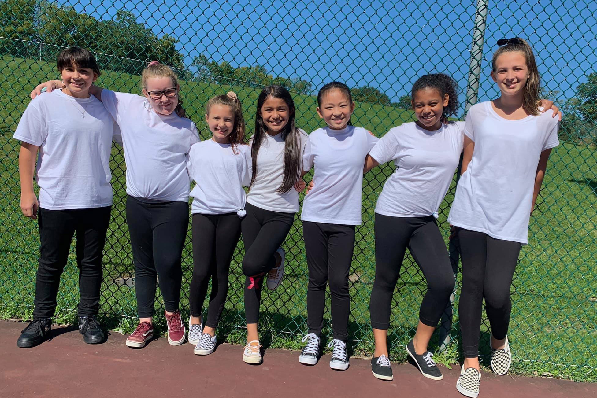 seven girls all wearing white t-shirts and black pants