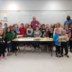Hudson Talbott poses with third grade students and Dr. Cook at table with his books
