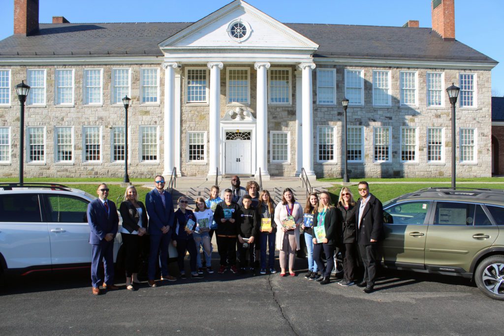 students, teachers, administratos, and Lacy family members pose with books and cars in front of Catskill Middle School