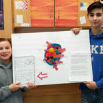 two boys hold up poster with 3D cell on it