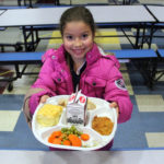 girl holding up cafeteria tray full of food