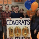 Jesse Davies and coaches holding up sign that says Congrats 100 wins Jesse!