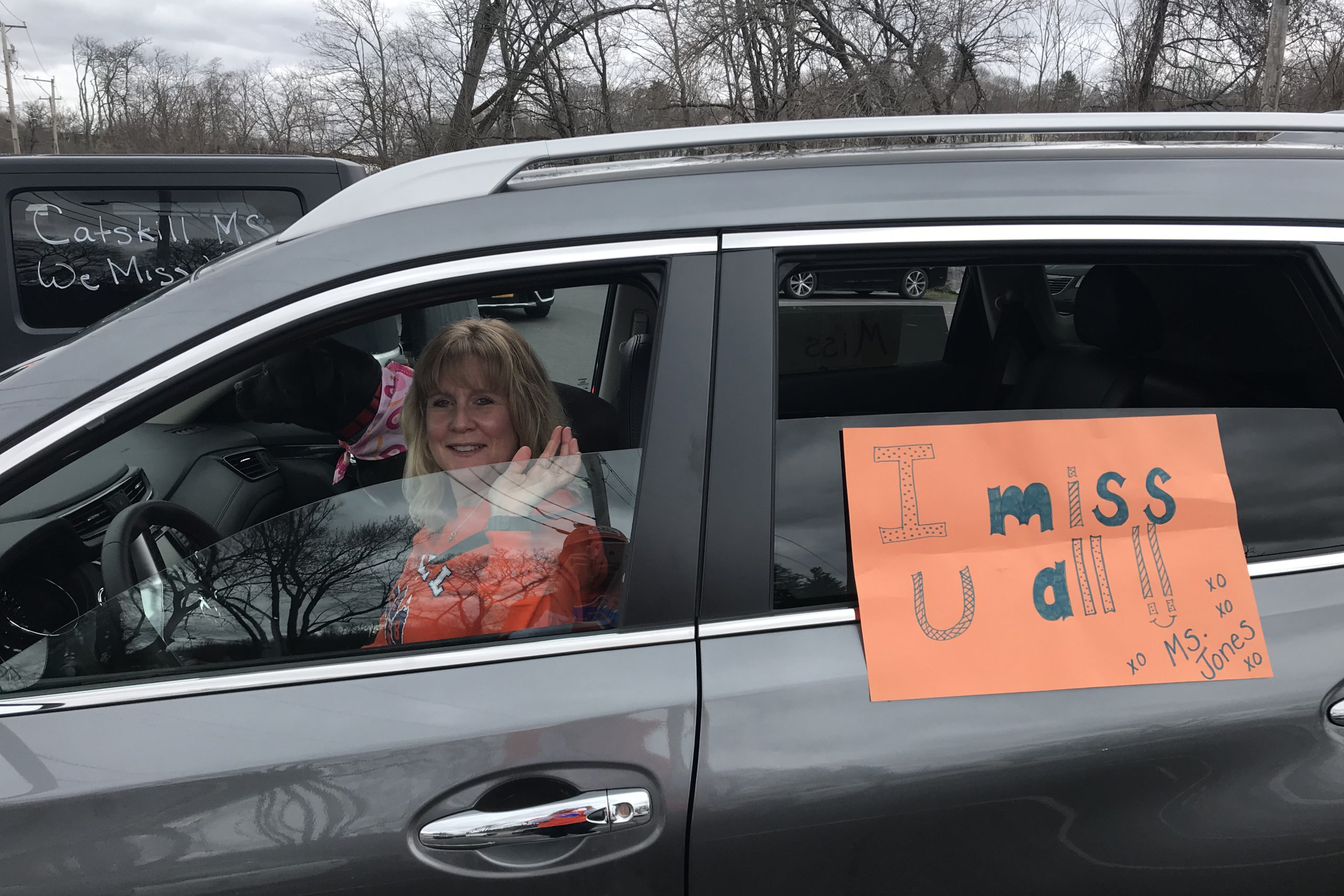 dog and woman in car with sign that says Miss U Guys