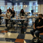women wearing masks in cafeteria with tables of school supplies