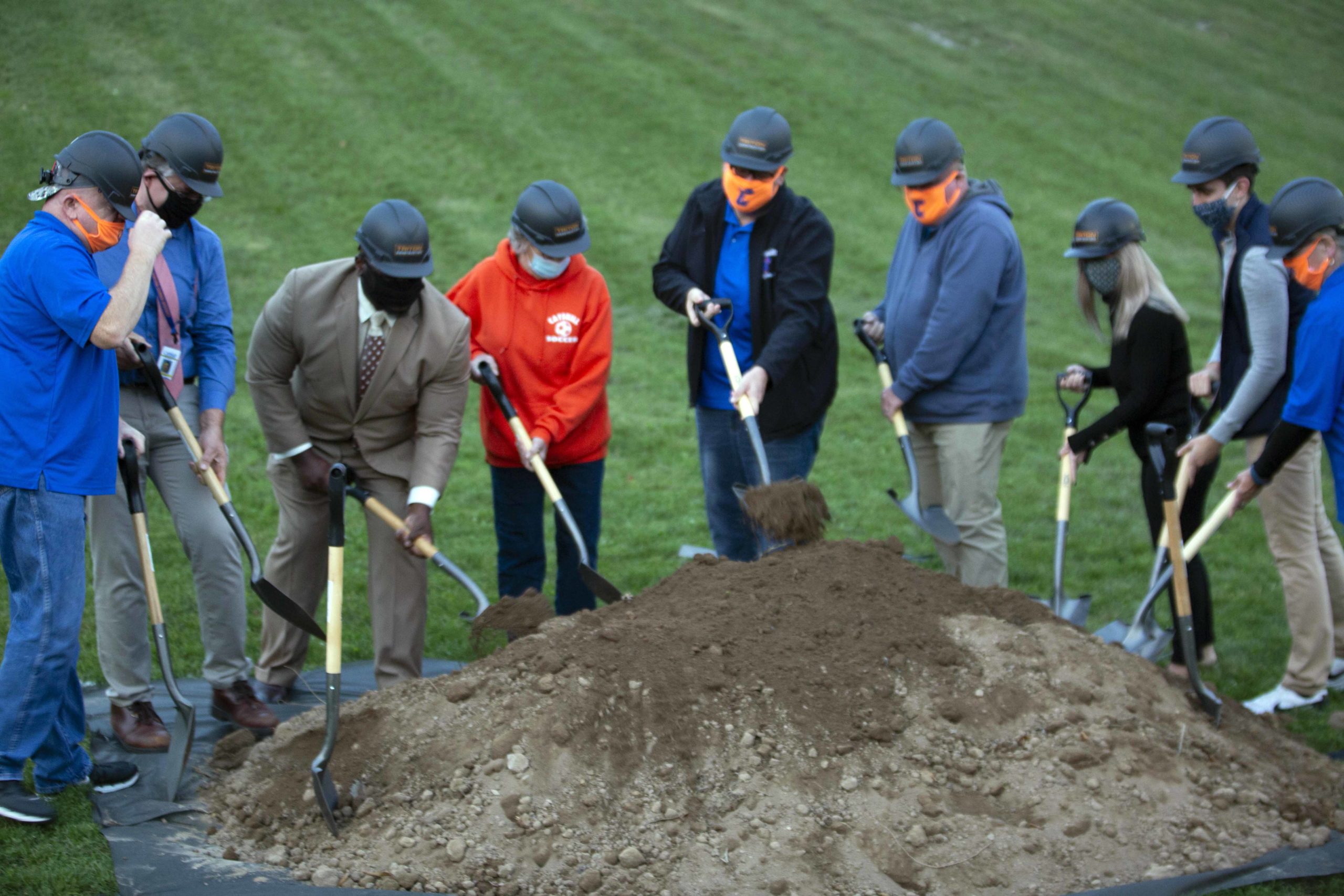 People wearing masks and hardhats shoveling dirt pile