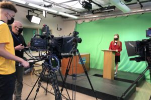 boy and man in school studio filming girl in red jacket