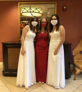 two girls in white dresses posing with girl in red dress