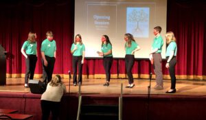 seven students wearing green shirts on stage