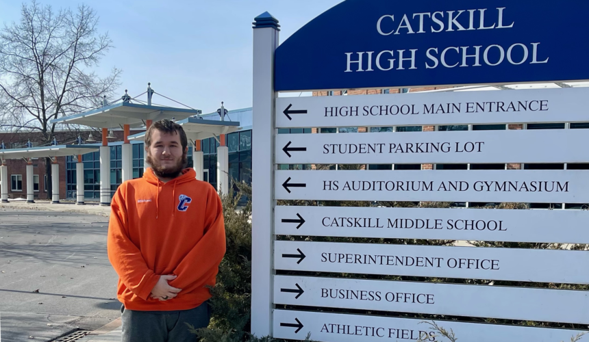 young man standing next to Catskill High School Sign