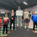 Daniael Forbes stands atop podium with five other wrestlers