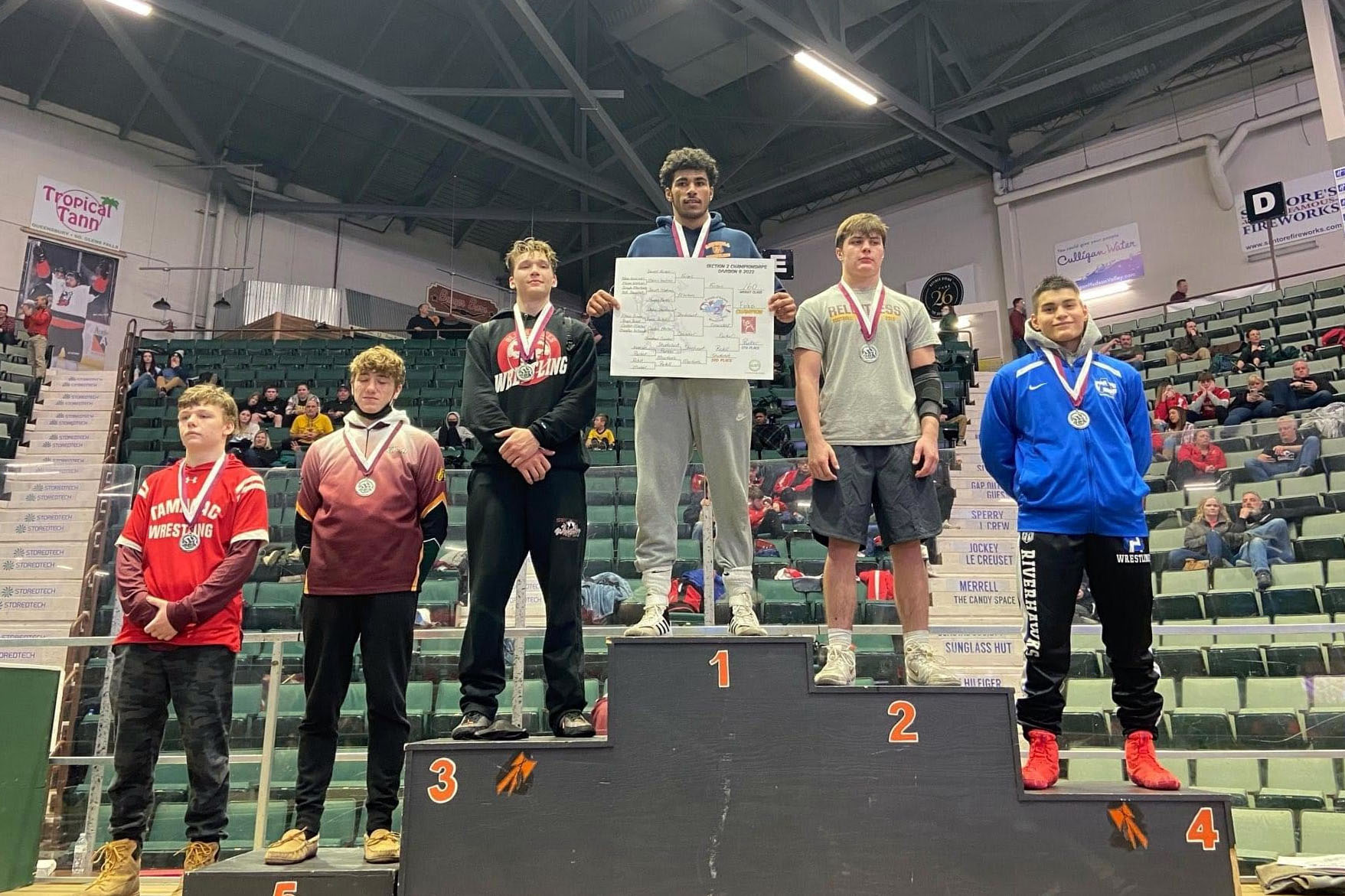 Daniael Forbes stands atop podium with five other wrestlers