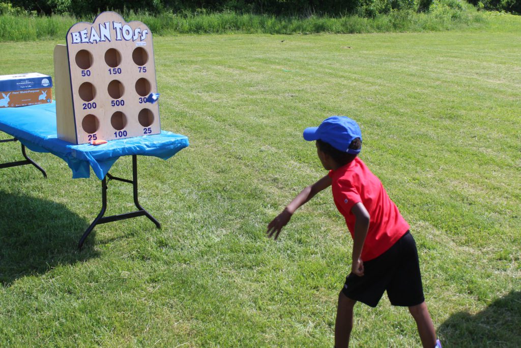 boy tossing bean bag at board with holes in it