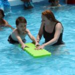teacher helping girl swim with pool float
