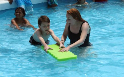 teacher helping girl swim with pool float