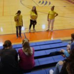 three girls in yellow shirts talking to students in bleachers.