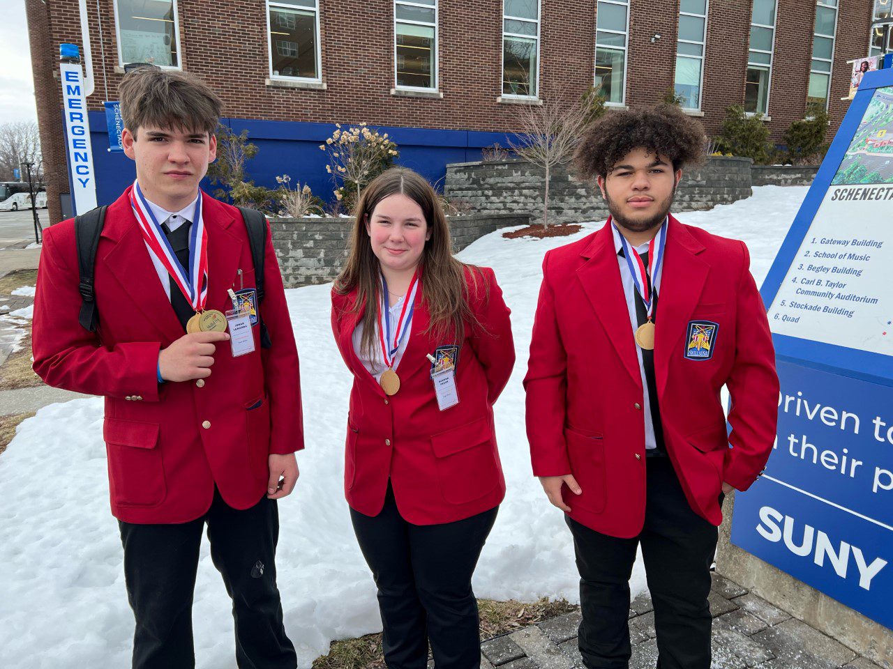 three students wearing red jackets and medals
