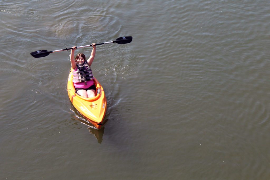 girl in kayak holding paddle over head