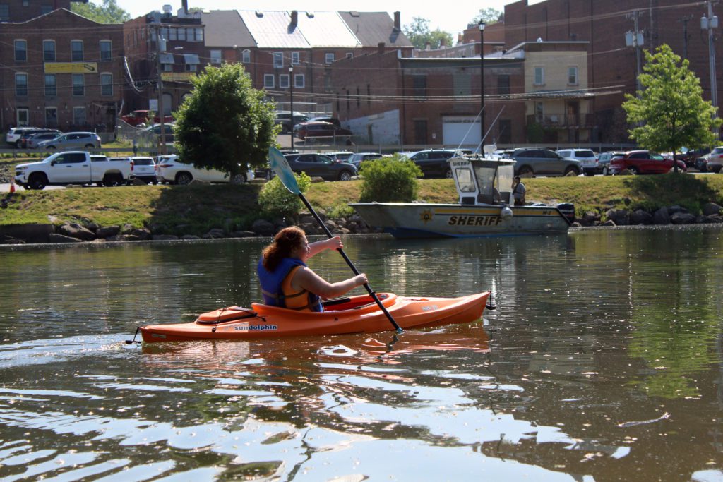 student paddling kayak past sheriff's boat