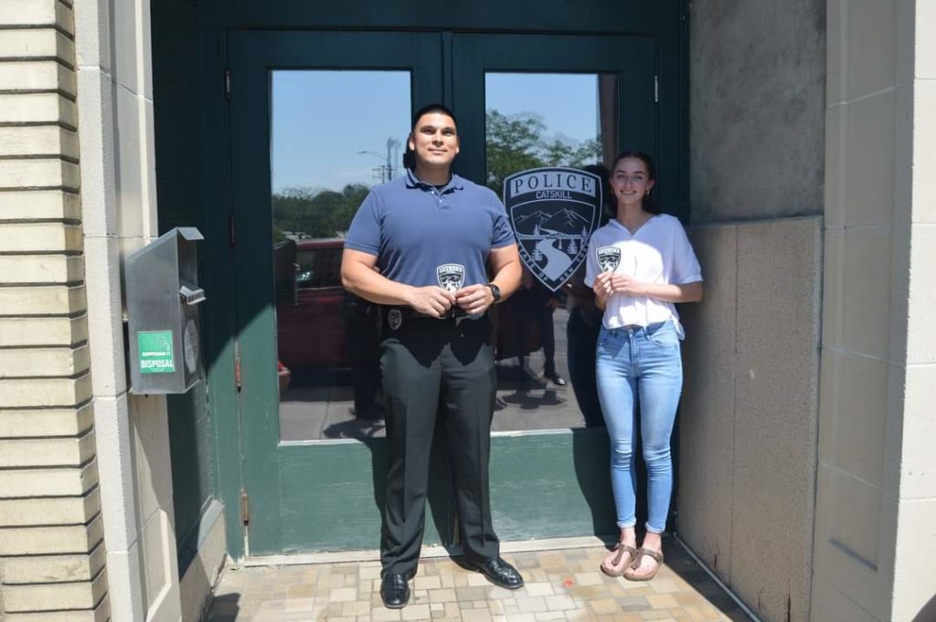 police officer and teenage girl pose next to Catskill Police Patch on police department door