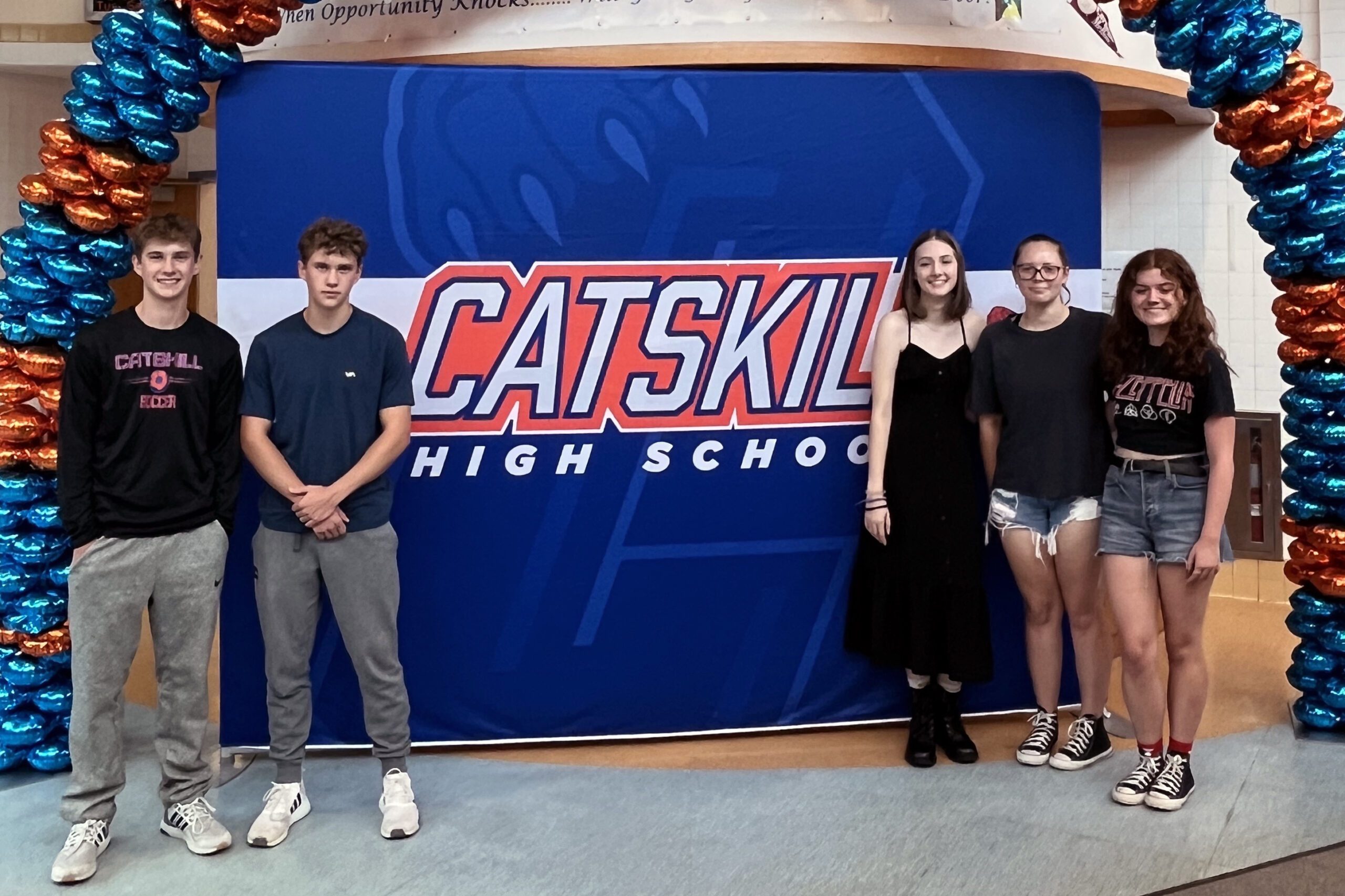 two boys and three girls of high school age standing next yo Catskill High School banner.