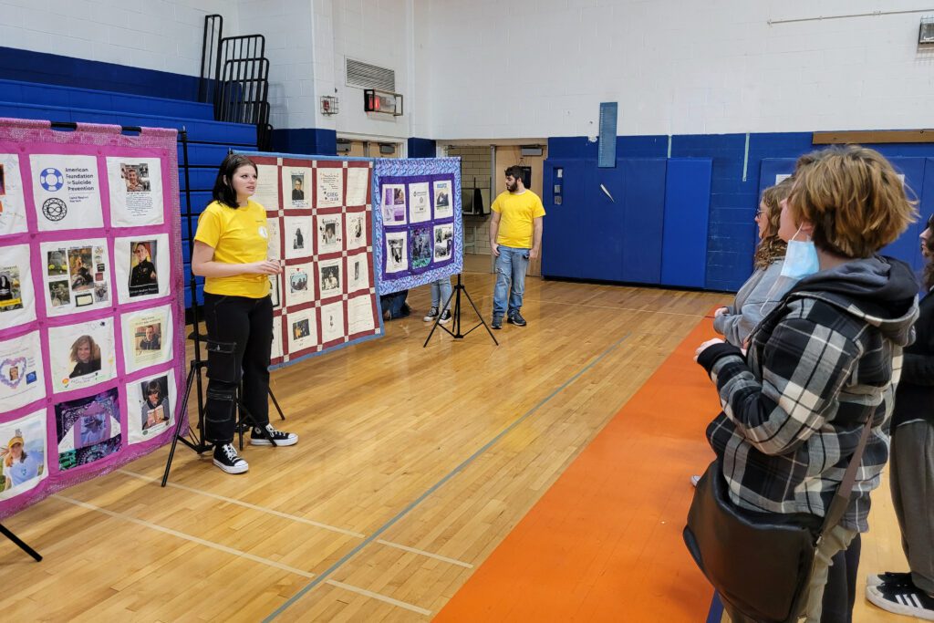 two strudenmt in yellow shirts showing quilts to group of students