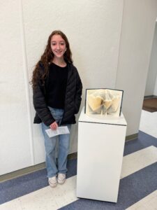 high school student standing next to book cutout art.