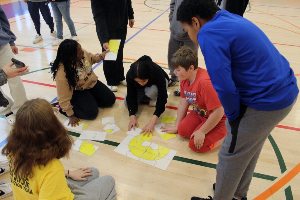middle school students putting together yellow ribbon puzzle on gym floor.