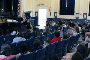 Woman talks in front of audience of fifth graders in auditorium