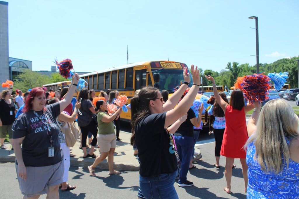 staff wave to buses leaving elementary school parking lot.