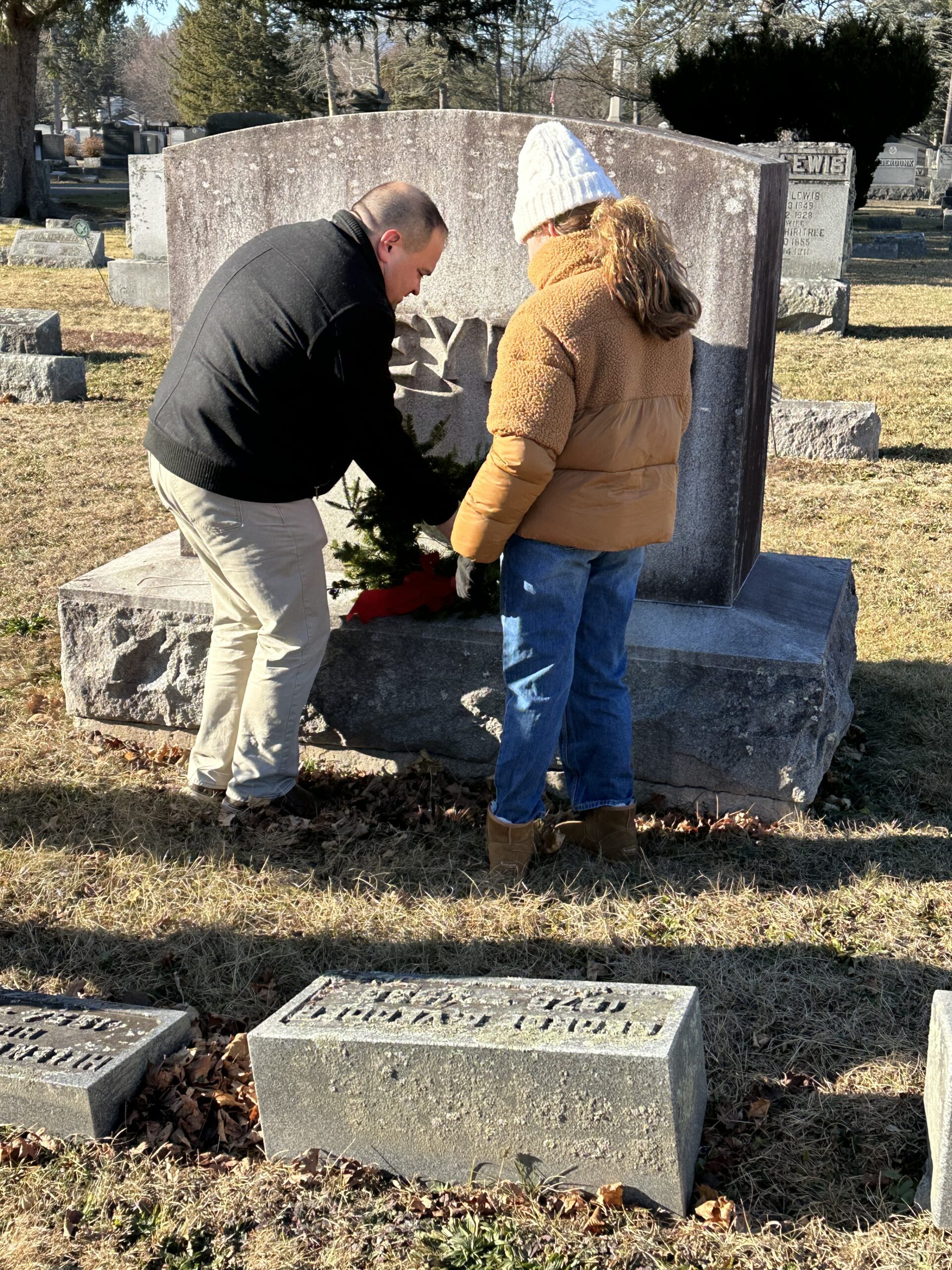 man and girl laying wreath on gravestone