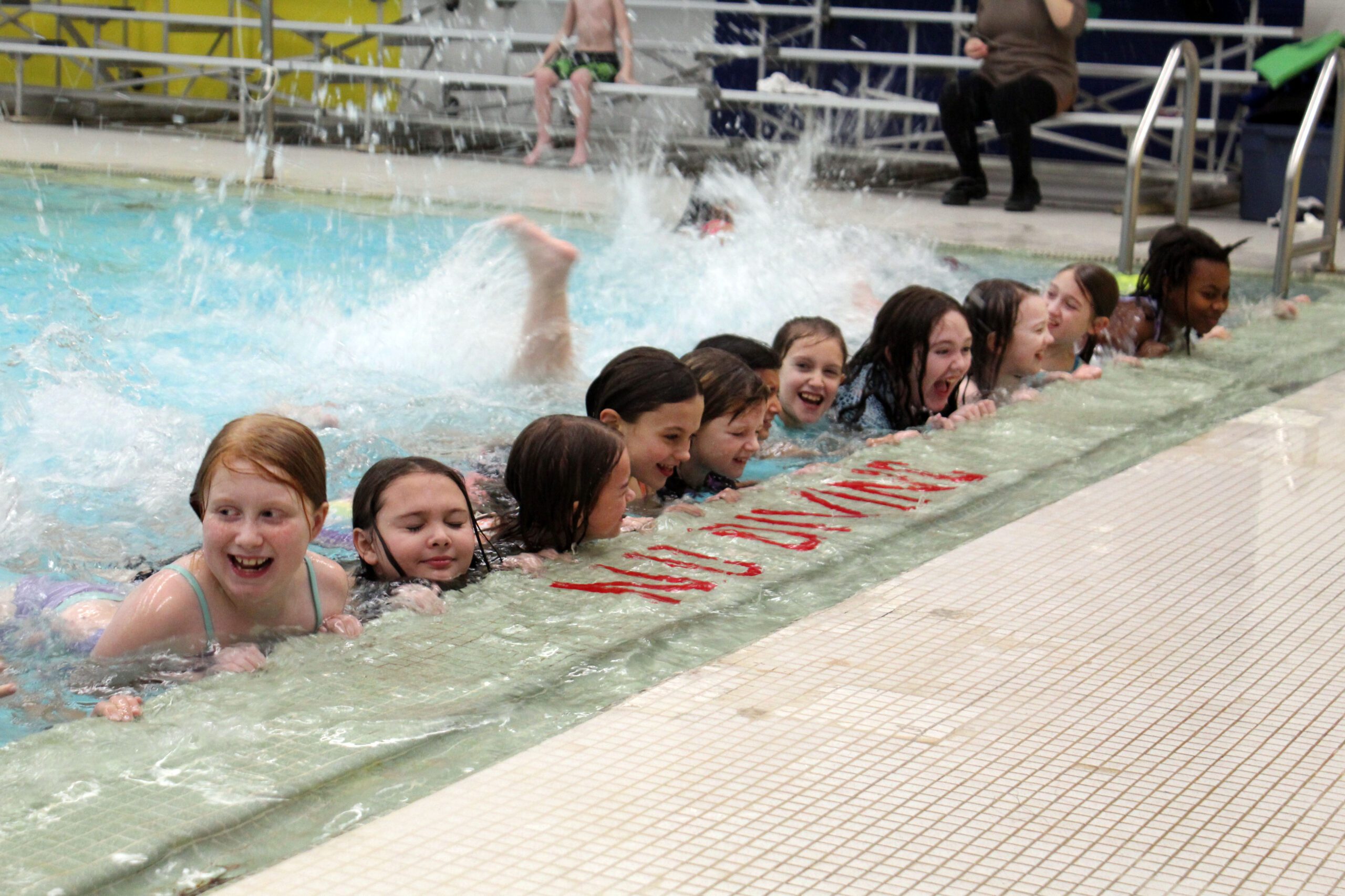 smiling kids holding onto edge of pool and kicking their legs