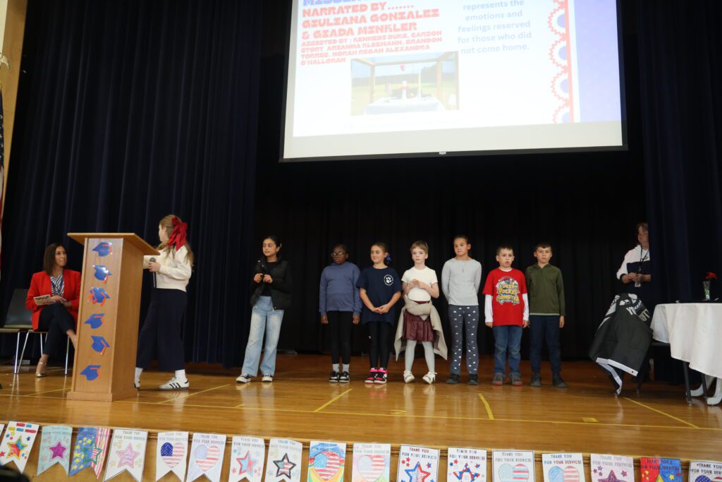 girl speaking at podium with students standing behind her on the stage