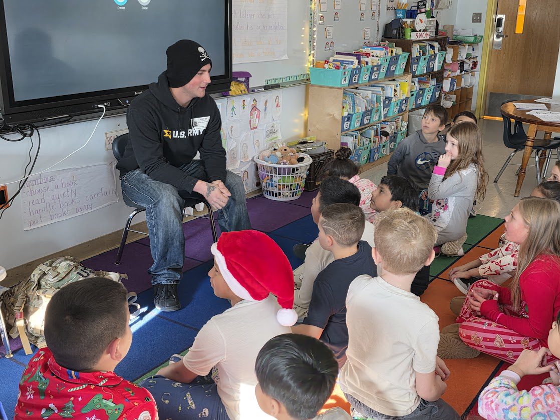 young man speaking to classroom of second graders seated on the floor