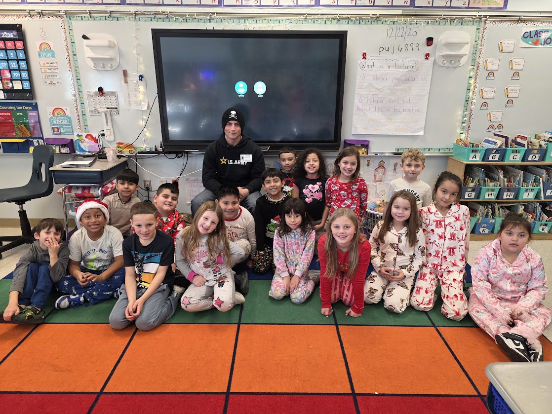 young man and second grade classes pose for photo together in classroom