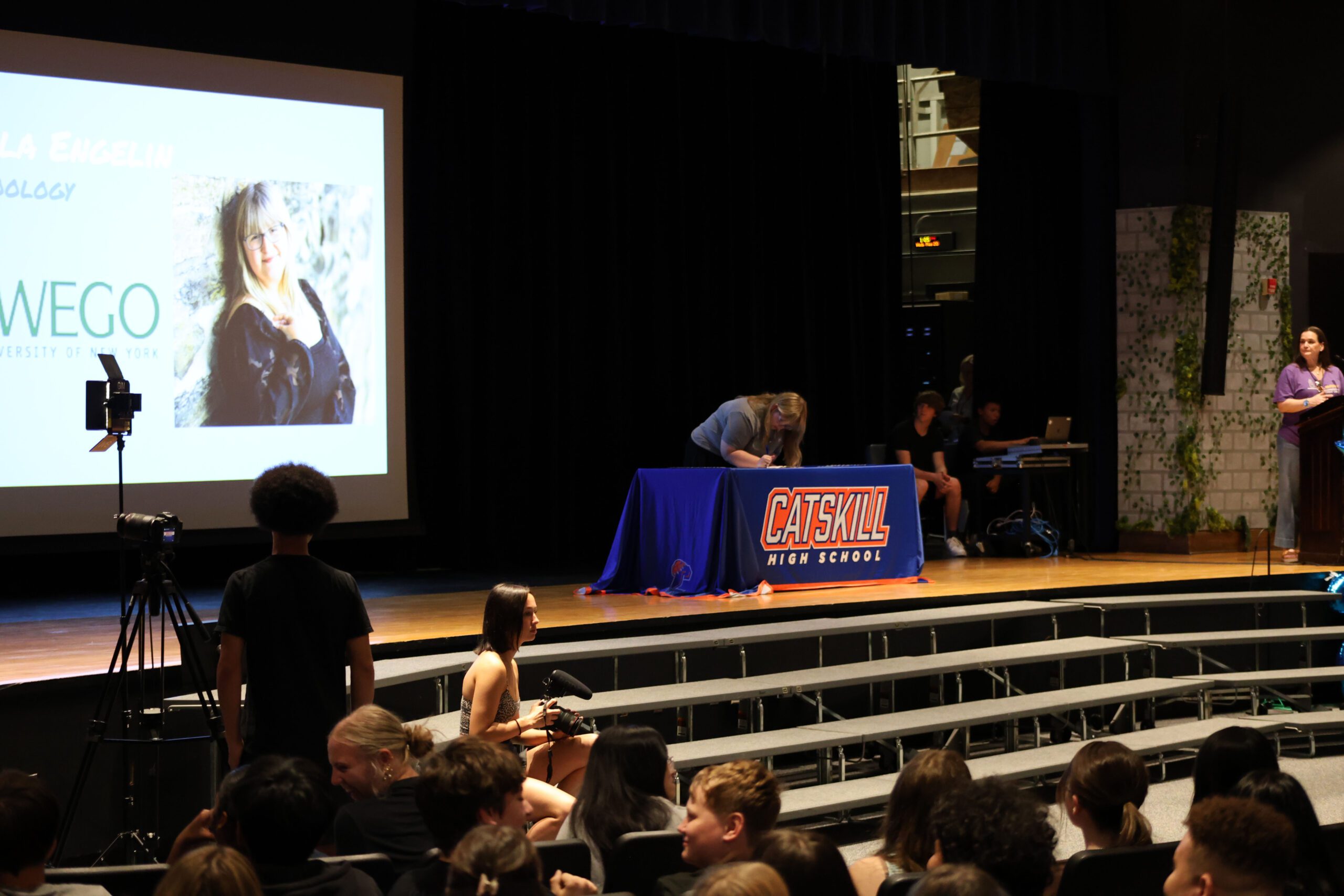 student signing letter at table on stage