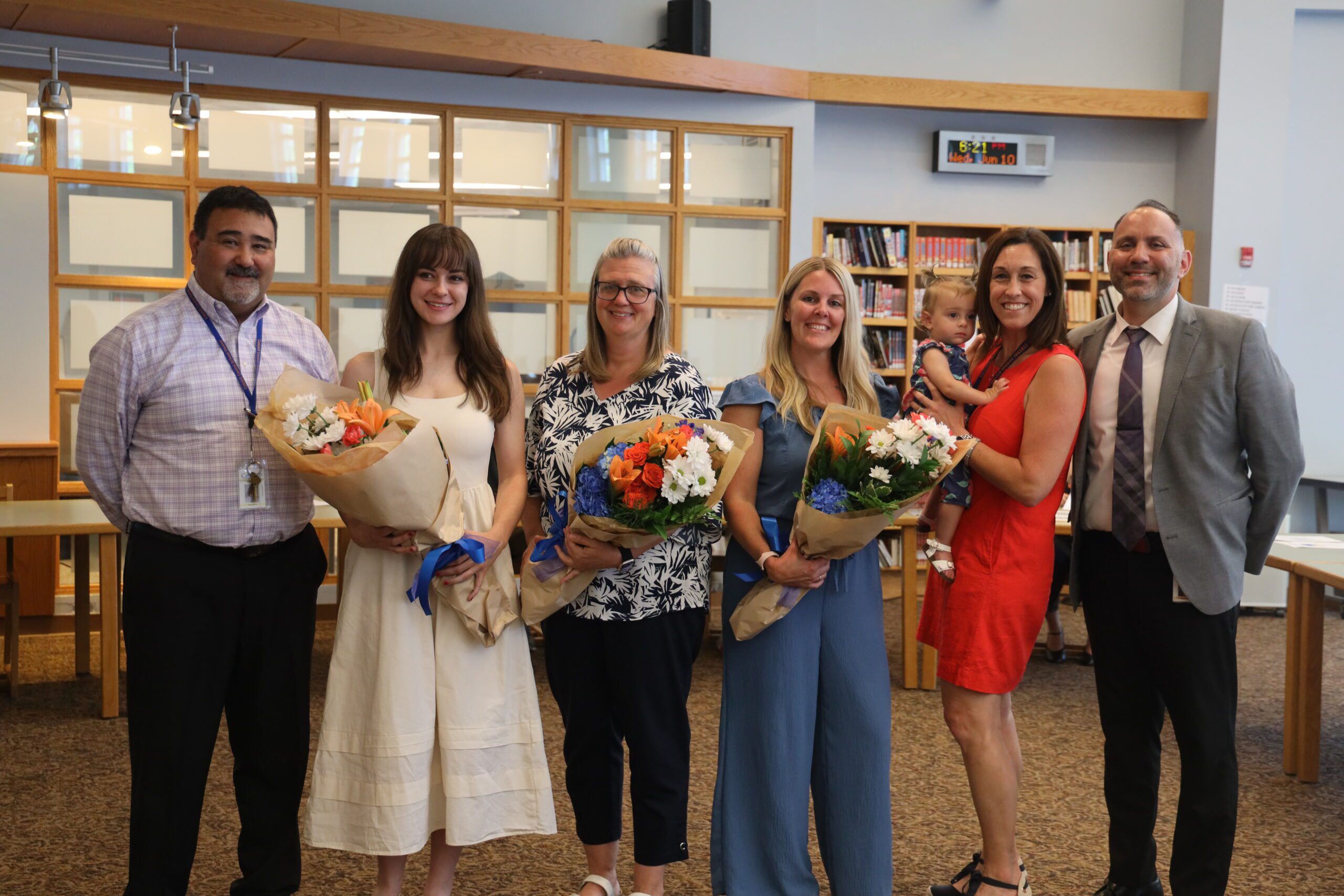 thre women holding flowers pose with school adminstrators