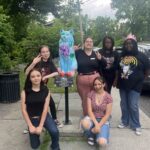 group of girls pose with Cat statue with trees and flowers painted on it