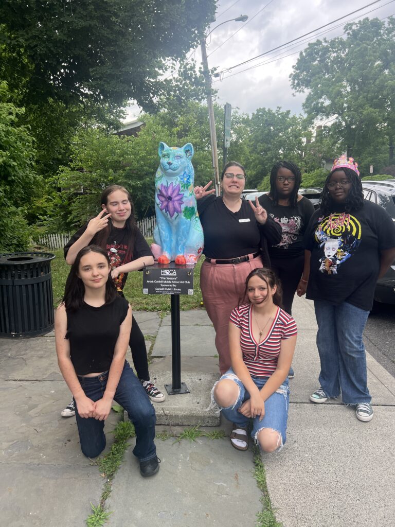 group of girls pose with Cat statue with trees and flowers painted on it