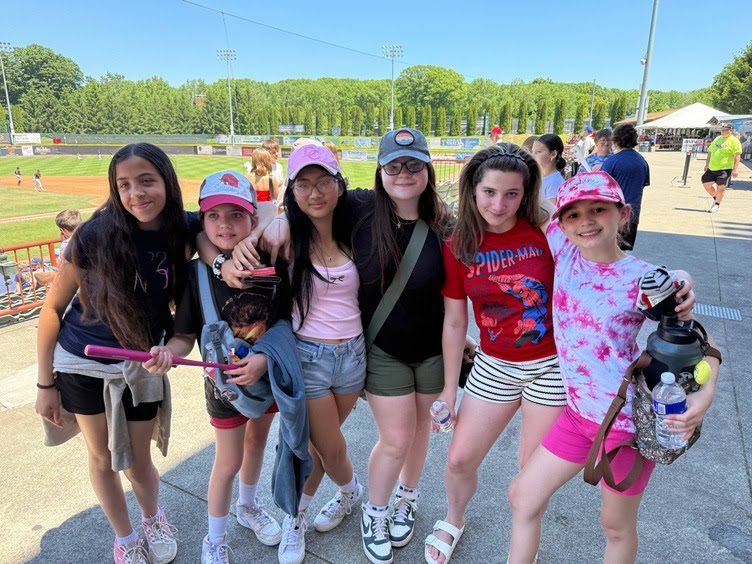 six girls pose for photo in from of baseball field